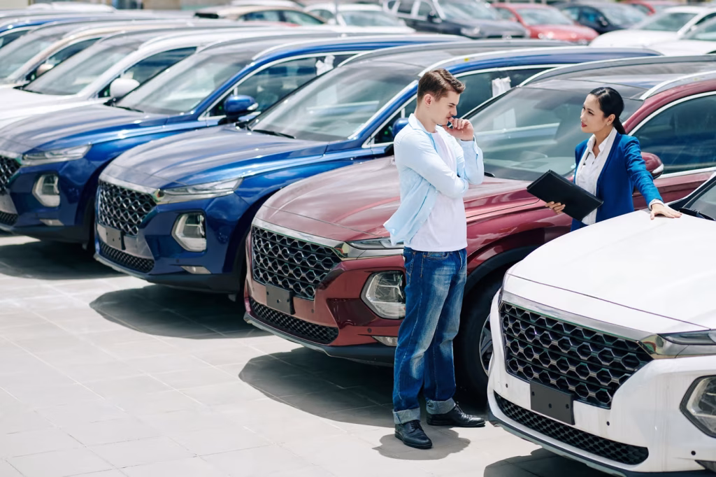 A car salesman and a buyer discuss options at a dealership, surrounded by SUVs. Ideal for those seeking cheap car rental Dubai.